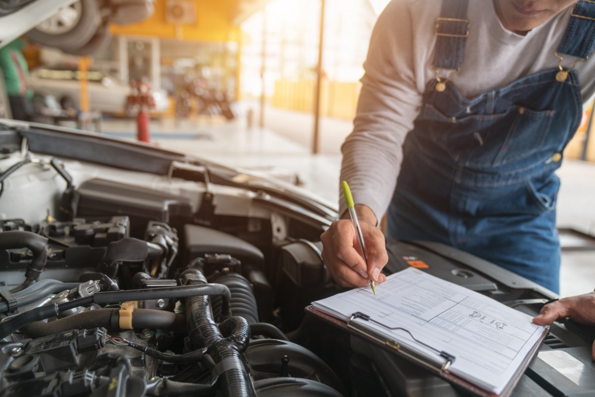 mechanic checking list with car hood up 