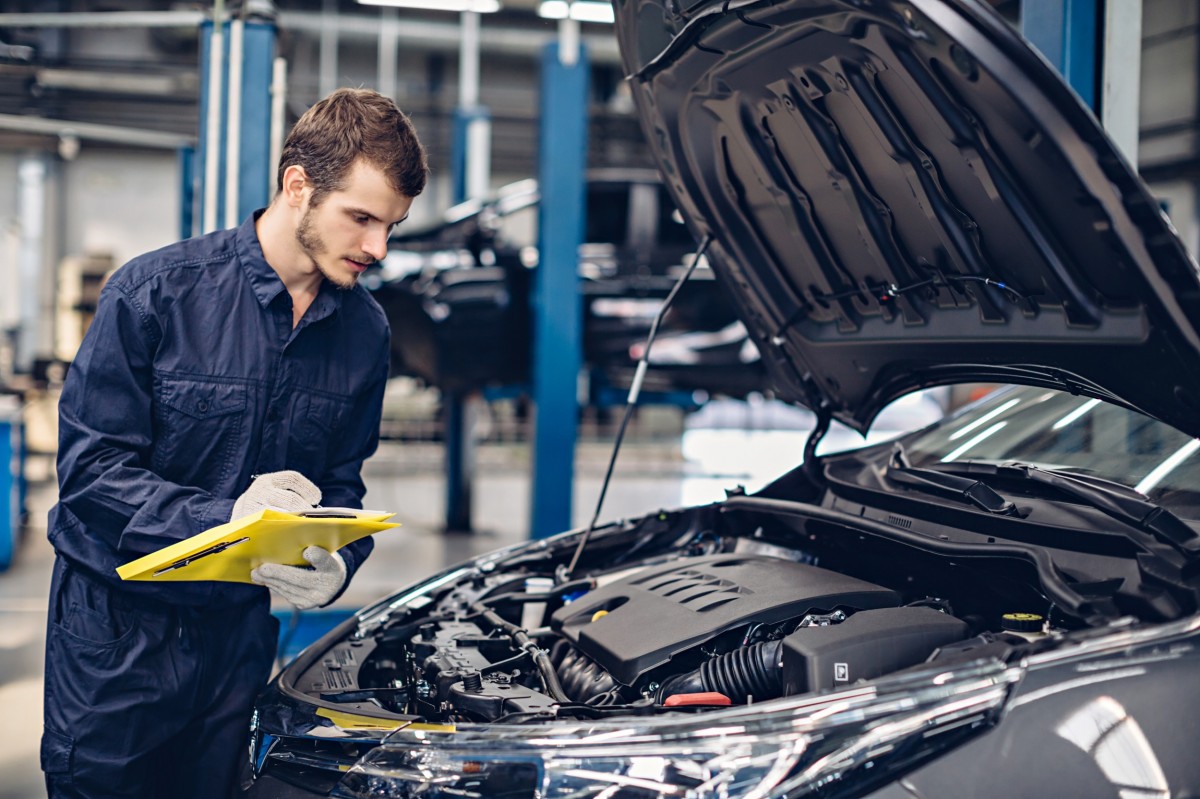 Man with clipboard checking under hood of car 